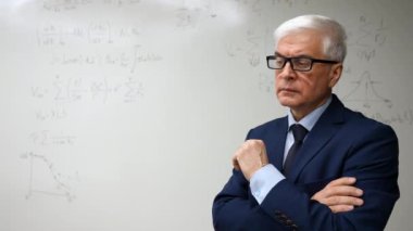 Olgun bir adam yazılı formüllerle beyaz bir tahtanın önünde duruyor.