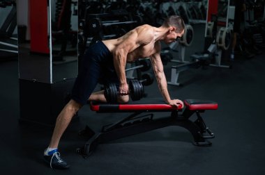 Gömleksiz bir adam spor salonunda dambıl sırasına dizer.