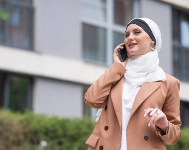 Açık havada akıllı telefondan konuşan tesettürlü genç kadın.