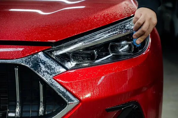 stock image A technician smoothes the vinyl film on a car headlight, removing air bubbles