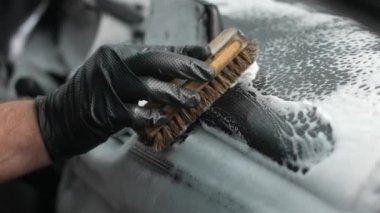 Bir tamirci arabanın içini fırça ve köpükle temizler.