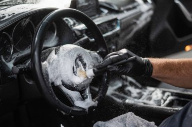 Bir tamirci arabanın içini fırça ve köpükle temizler.