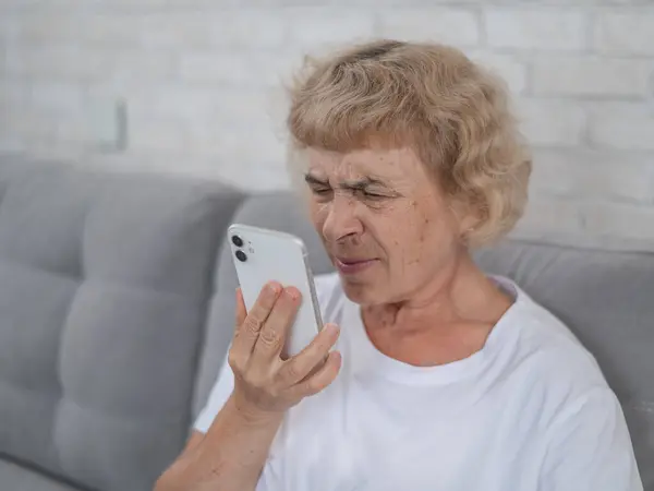 An elderly Caucasian woman suffers from myopia and tries to read a message on a smartphone