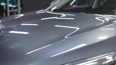 Bir adam gri bir arabanın yüzeyini mikrofiber bir bezle siliyor.