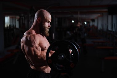 Beyaz, kel, üstsüz bir adam spor salonunda halterle egzersiz yapıyor. Ağırlıklarla bibik bukleler