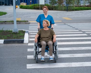 Kızıl saçlı hemşire yaşlı bir kadını yolun karşısına itiyor.