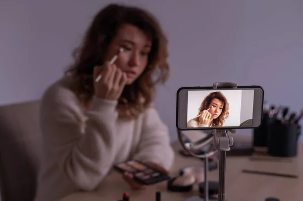 Caucasian woman leads an online make-up lesson for herself on her mobile phone.