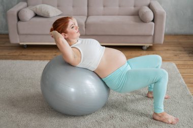 Hamile kızıl saçlı kadın evde spor yapıyor.