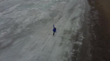 Donmuş bir gölde mavi kazak giyen bir kadının hava görüntüsü. Artistik patinajcı programı gerçekleştirir