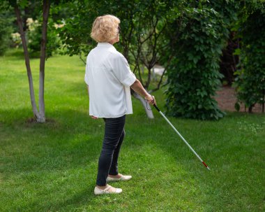 Yaşlı kör kadın parkta yürüyor.