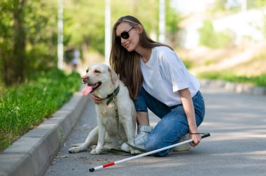 Dışarıda yürürken rehber köpeğe sarılan kör genç bir kadın.