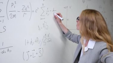 Genç bilim kadını beyaz tahtaya formüller yazıyor.