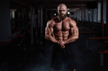 Tişörtsüz poz veren kaslı kel adam. Vücut geliştirici spor salonunda vücudunu gösteriyor.