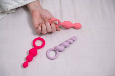 Bir kadın yatakta yatarken bir setten anal boncuk seçer.