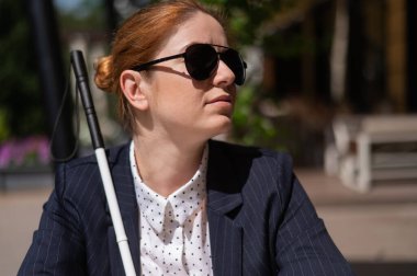 Takım elbiseli kör bir kadın açık bir kafede oturuyor.