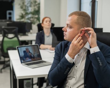 Kafkasyalı adam bilgisayardaki online toplantıya işitme cihazı koyuyor.