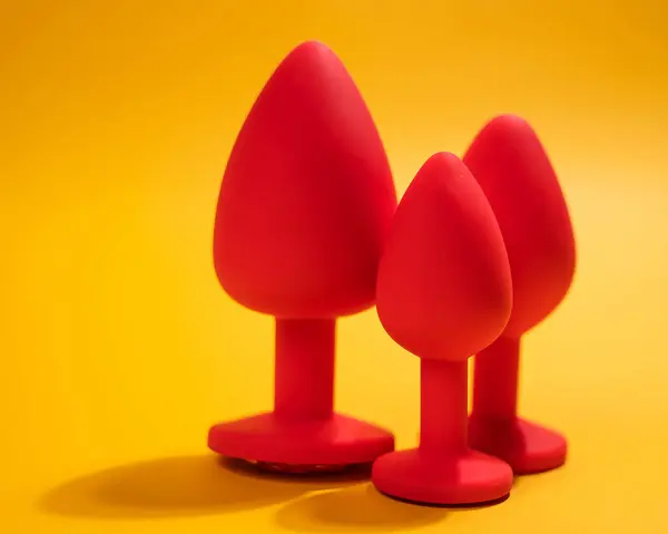 Three size silicone red butt plugs on an orange background