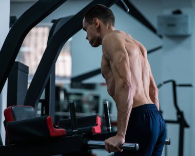 Shirtless man doing triceps dips from parallel bars in gym