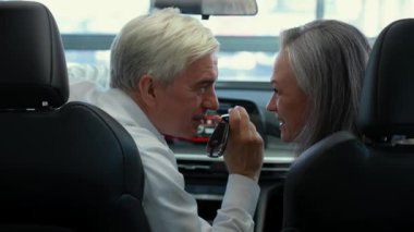 Olgun bir beyaz çift yeni bir arabada oturuyor. Arabanın anahtarlarını tutan yaşlı bir adam.