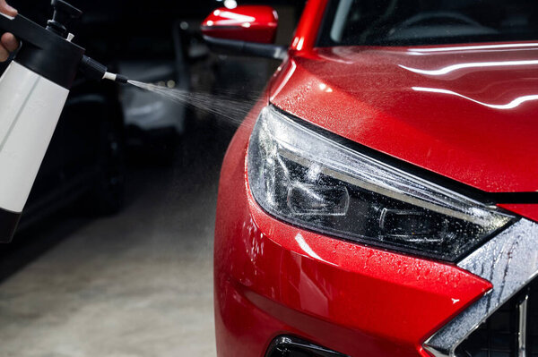 Мужчина моет фары красной машины спреем