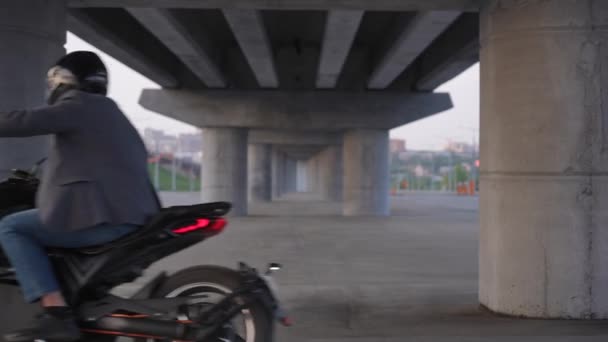 ジャケットとヘルメットの男が橋の下で電動バイクに乗る — ストック動画