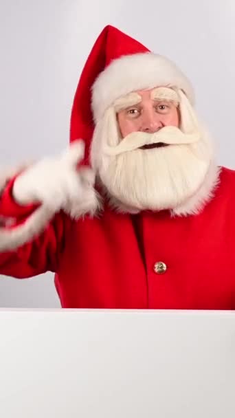 サンタクロースはホワイトボードの後ろから外を見て指を指差します バーティカルビデオ — ストック動画