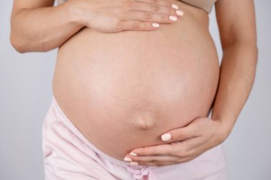 Üçüncü üç aylık dönemde hamile kadınların göbeğine beyaz arka planda yakın çekim.