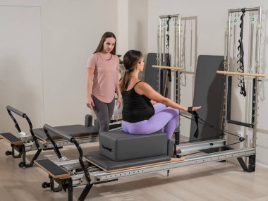 Kafkasyalı hamile kadın, bireysel bir eğitmenle ıslah makinesinde pilates egzersizi yapıyor.