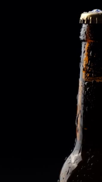 一瓶由深色玻璃杯制成的啤酒在黑色的背景上旋转 垂直录像 — 图库视频影像