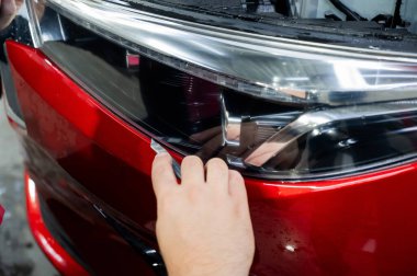 Usta, kırmızı bir arabanın farına vinil film uyguluyor.