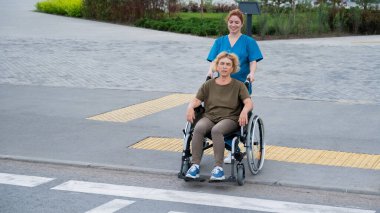 Kızıl saçlı hemşire yaşlı bir kadını yolun karşısına itiyor.