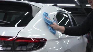 Bir tamirci mikrofiber bezle beyaz bir arabanın vücudunu siler.