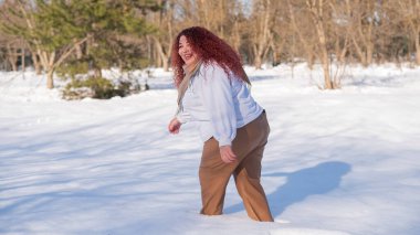 A fat red-haired woman in a white sweatshirt walks through snowdrifts