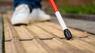 Kör bir kadın, sarı kiremitler üzerinde sokakta yürüyor. Dokunsal bastona odaklan.