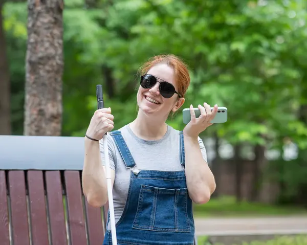 Happy blind pregnant woman sitting on bench and talking on smartphone