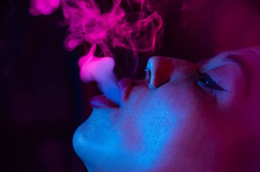 Kısa saçlı, neon ışıkta sigara içen Asyalı kadının yakın portresi.