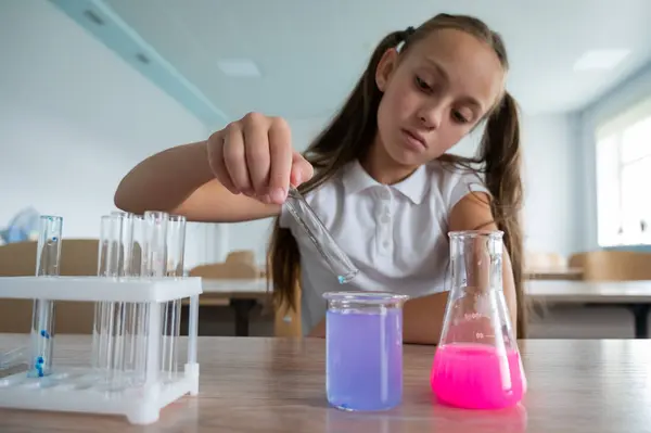 stock image A schoolgirl conducts experiments in a chemistry lesson. Girl pouring colored liquids from a beaker