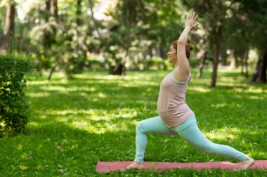 Parkta yoga yapan hamile, beyaz bir kadın. Savaşçı Pozisyonu