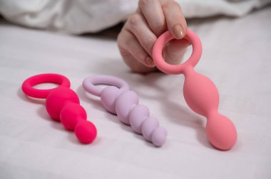 Bir kadın yatakta yatarken bir setten anal boncuk seçer.