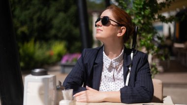 Takım elbiseli kör bir kadın açık bir kafede oturuyor.