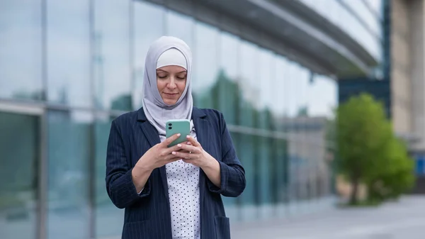 Business woman in hijab and suit using smartphone outdoors