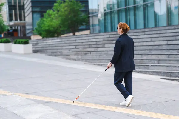 Blind businesswoman walking along tactile tiles with a cane