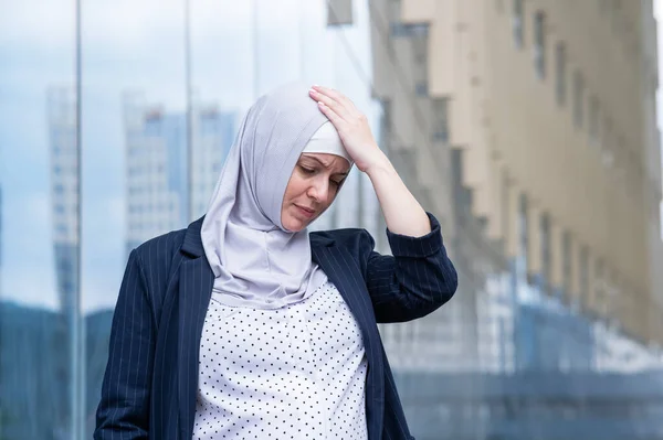 Portrait of sad business woman in hijab and suit outdoors
