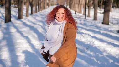 Portrait of an excited red-haired curly fat woman in the park in winter