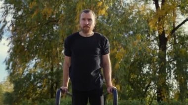 Beyaz adam sonbaharda açık havada paralel barlarda egzersiz yapıyor. Yavaş çekim