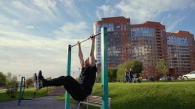 Kafkas sakallı bir adam bacaklarını kaldırırken açık havada yatay bir barda asılı duruyor.