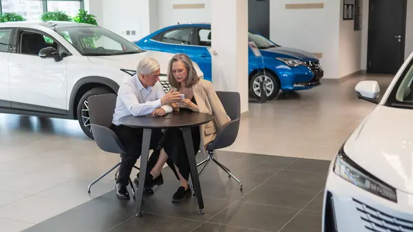 Dojrzała Para Siedzi Salonie Samochodowym Patrzy Smartfona — Zdjęcie stockowe