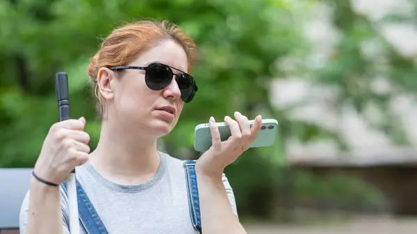 A blind woman sits on a bench and communicates on a smartphone