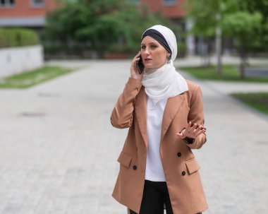 Açık havada akıllı telefondan konuşan tesettürlü genç kadın.