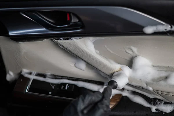 A man cleans the interior of a car with foam and a brush. Clean the door trim